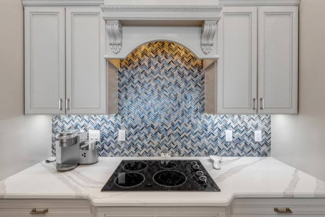 kitchen with gray cabinetry, backsplash, black electric stovetop, and light stone counters