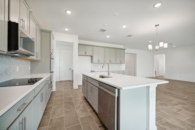 kitchen with tasteful backsplash, stainless steel appliances, a center island with sink, sink, and gray cabinets