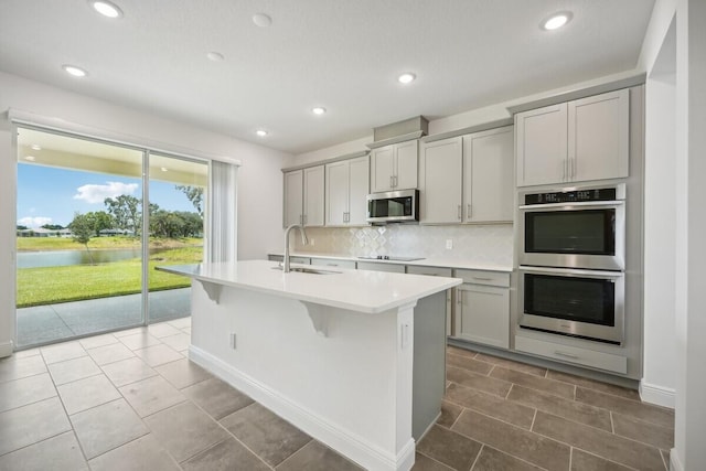 kitchen with light tile patterned floors, backsplash, a water view, appliances with stainless steel finishes, and sink