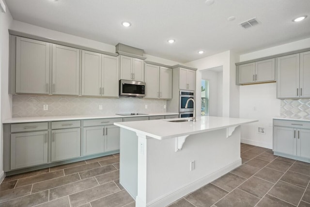 kitchen with tile patterned floors, tasteful backsplash, stainless steel appliances, a kitchen island with sink, and gray cabinetry