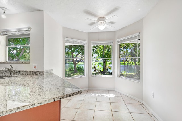 interior space with ceiling fan, light tile patterned flooring, light stone counters, and a textured ceiling