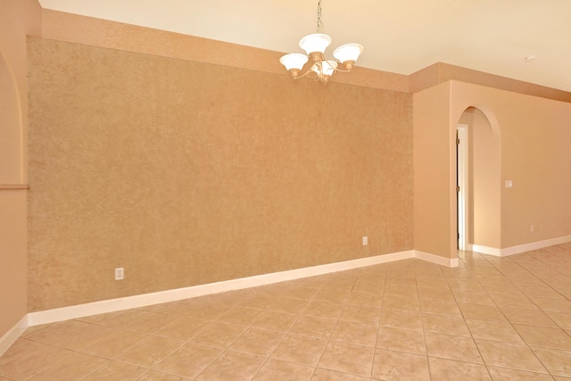 tiled spare room featuring an inviting chandelier