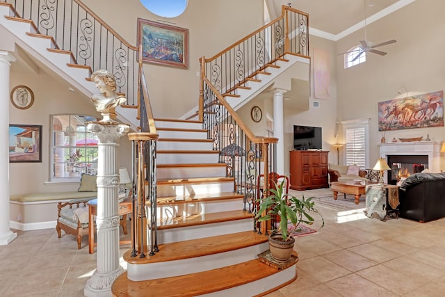 stairs with decorative columns, crown molding, a healthy amount of sunlight, and a high ceiling