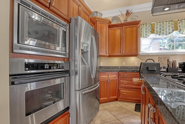 kitchen with dark stone countertops, light tile patterned floors, stainless steel appliances, and ornamental molding