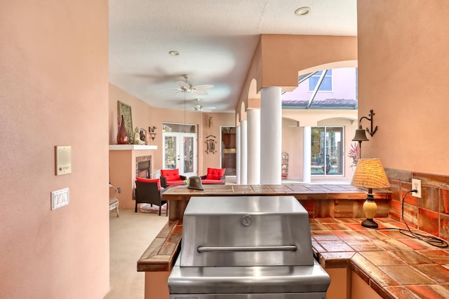 kitchen with light carpet, tile countertops, ceiling fan, and a fireplace