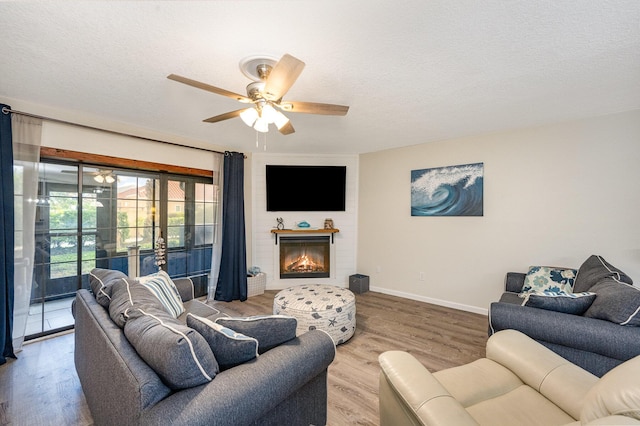 living room featuring a fireplace, wood-type flooring, a textured ceiling, and ceiling fan