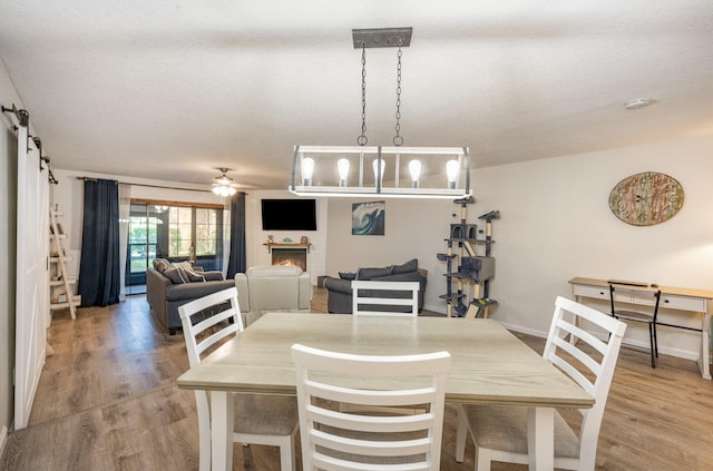 dining space with wood-type flooring, a barn door, a textured ceiling, and ceiling fan