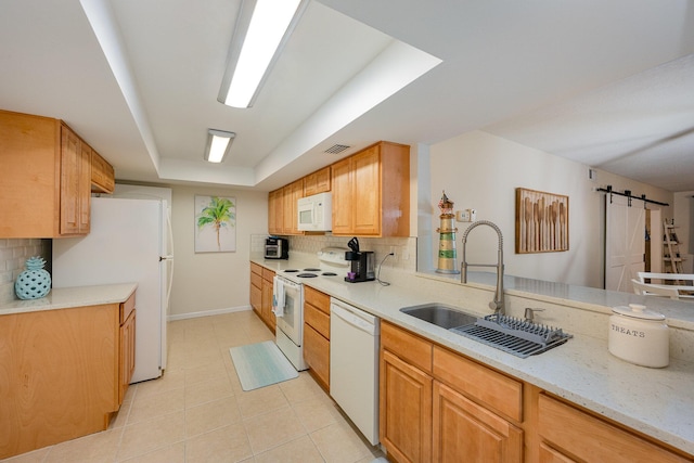 kitchen featuring sink, a raised ceiling, a barn door, white appliances, and decorative backsplash