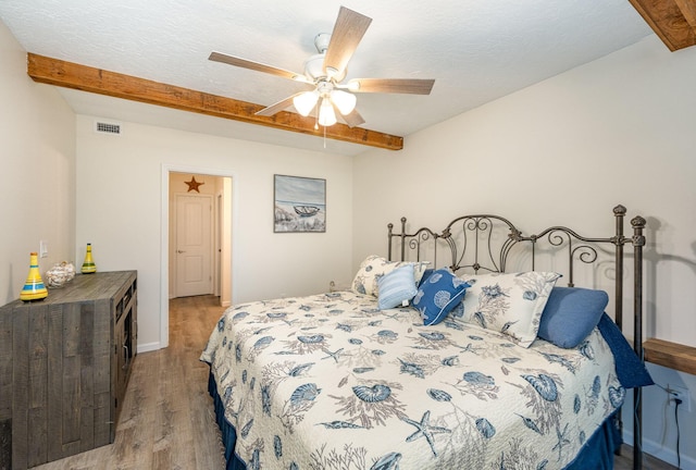 bedroom with beamed ceiling, a textured ceiling, light wood-type flooring, and ceiling fan