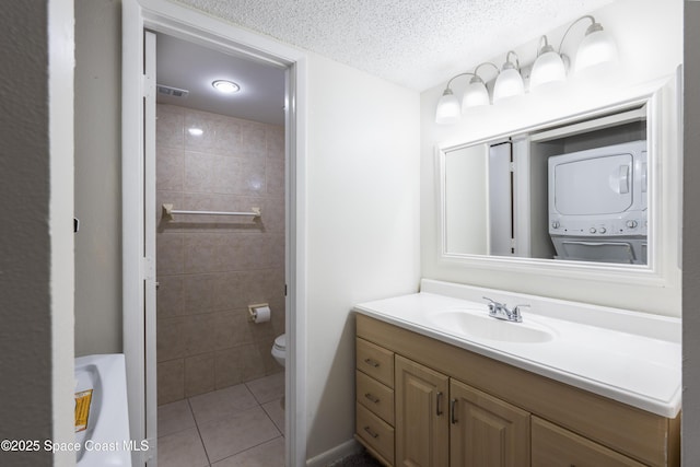 bathroom featuring tile patterned flooring, a textured ceiling, toilet, vanity, and stacked washer and clothes dryer