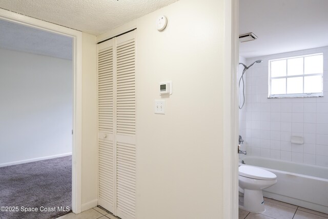 bathroom with tile patterned flooring, a textured ceiling, tiled shower / bath combo, and toilet