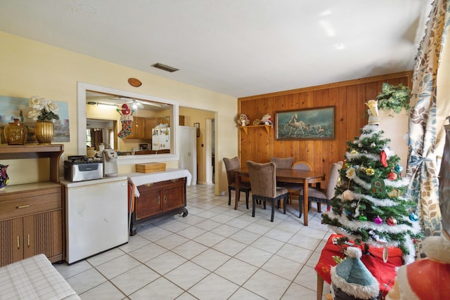 interior space with wood walls, ceiling fan, light tile patterned floors, and white fridge