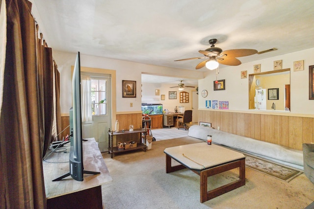 carpeted living room featuring wood walls and ceiling fan