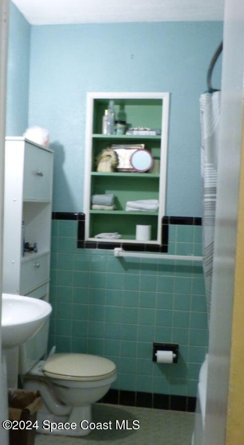 bathroom featuring toilet and tile walls