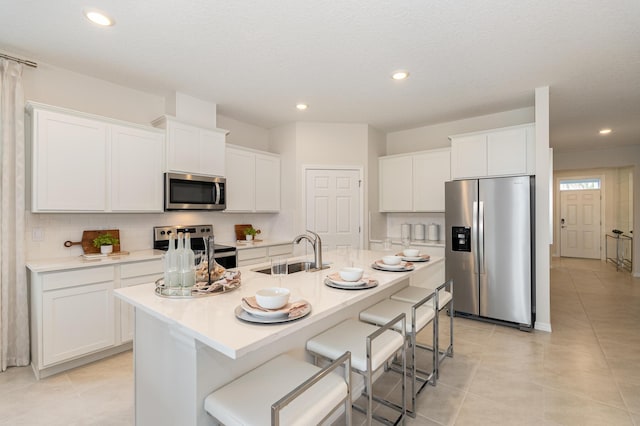 kitchen with sink, stainless steel appliances, a kitchen breakfast bar, white cabinets, and a center island with sink