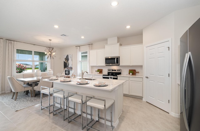 kitchen featuring pendant lighting, sink, white cabinetry, stainless steel appliances, and a center island with sink