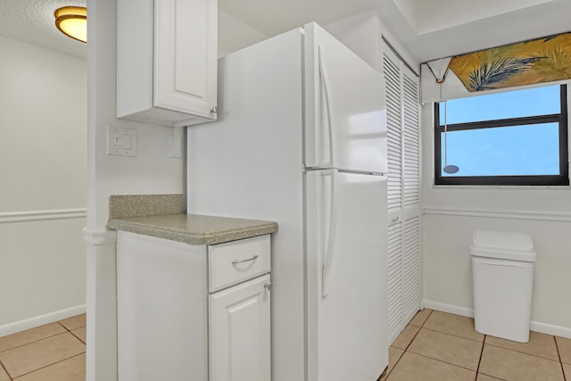 kitchen featuring a textured ceiling, white cabinets, light tile patterned floors, and white refrigerator