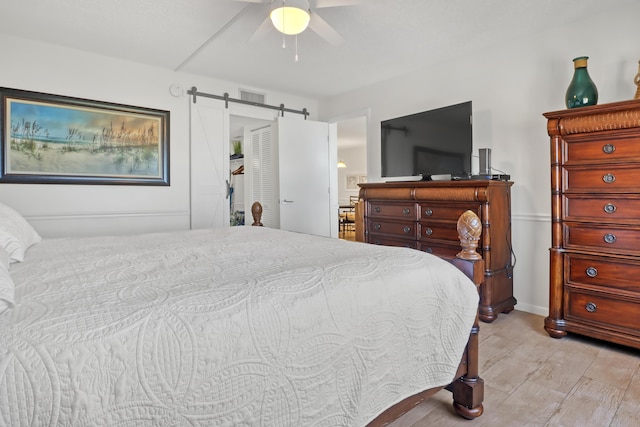 bedroom featuring a barn door, ceiling fan, and light hardwood / wood-style flooring