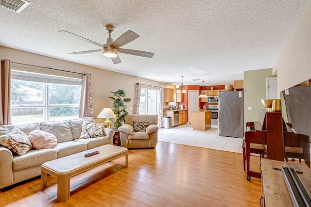 living room featuring light hardwood / wood-style flooring, ceiling fan with notable chandelier, and a textured ceiling