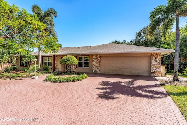 single story home with decorative driveway, a shingled roof, stone siding, and a garage