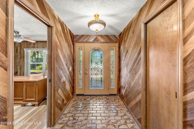 entryway featuring wooden walls, a textured ceiling, and ceiling fan