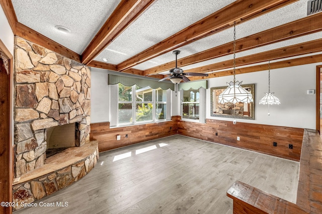 unfurnished living room featuring ceiling fan, wood walls, a textured ceiling, and light wood-type flooring