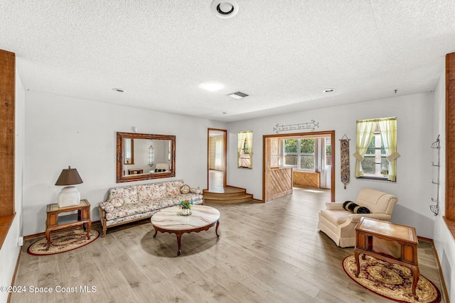 living area featuring a textured ceiling, baseboards, and light wood-style floors