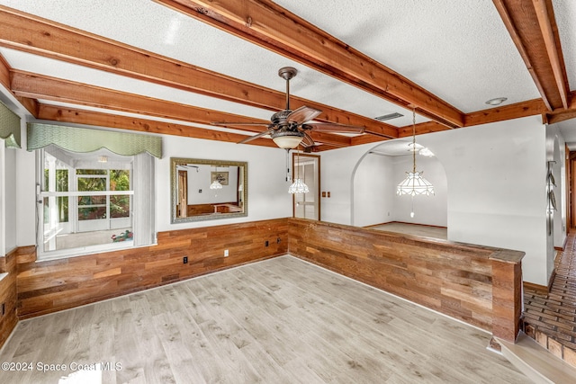 empty room featuring beamed ceiling, wooden walls, light wood-type flooring, a textured ceiling, and ceiling fan