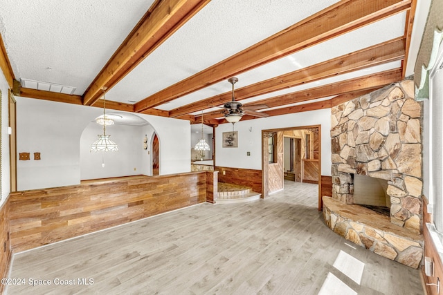 unfurnished living room featuring a stone fireplace, beam ceiling, light wood-type flooring, a textured ceiling, and ceiling fan