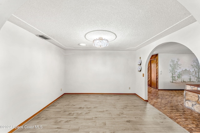 spare room with a textured ceiling, visible vents, arched walkways, wood finished floors, and baseboards