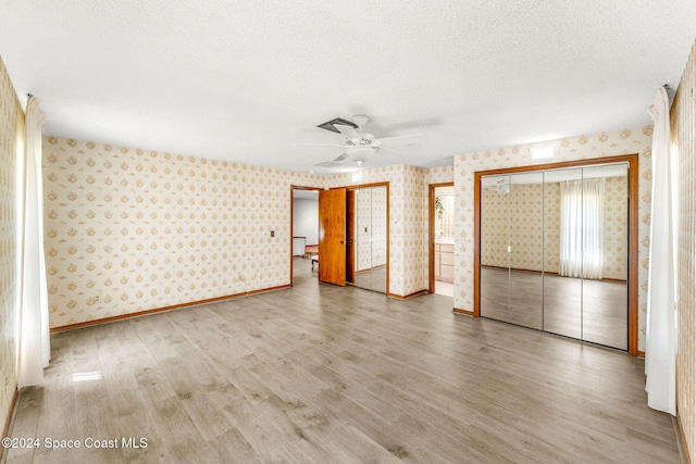 unfurnished bedroom with two closets, wallpapered walls, and wood finished floors