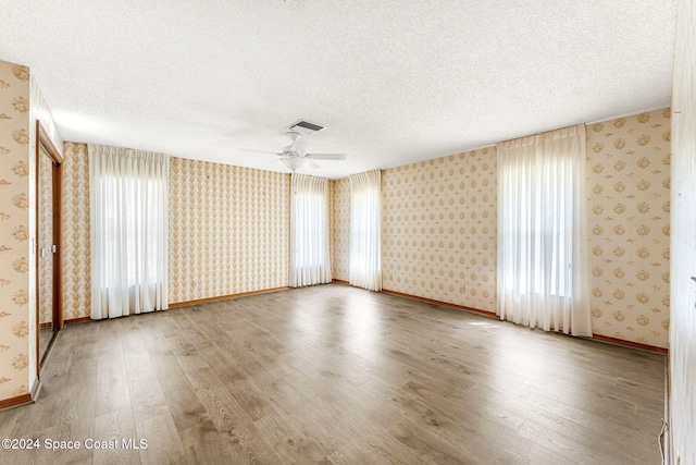 empty room featuring visible vents, a textured ceiling, wood finished floors, and wallpapered walls