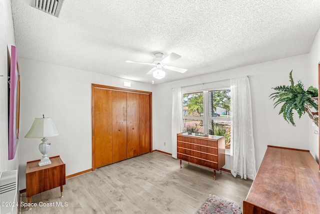 living area with a textured ceiling, light wood-type flooring, and ceiling fan