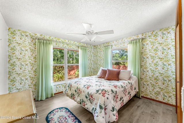 bedroom with a textured ceiling, multiple windows, wood-type flooring, and ceiling fan