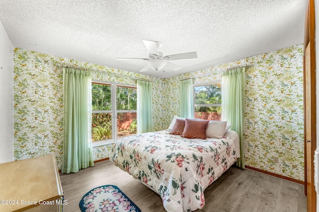 bedroom featuring baseboards, a textured ceiling, wallpapered walls, and wood finished floors