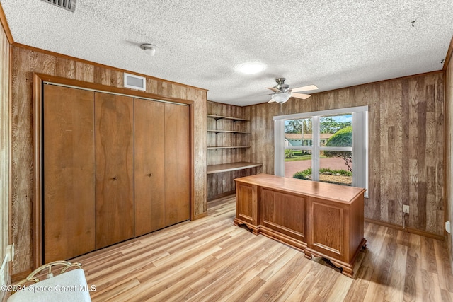 home office featuring a textured ceiling, ceiling fan, wooden walls, ornamental molding, and light hardwood / wood-style flooring