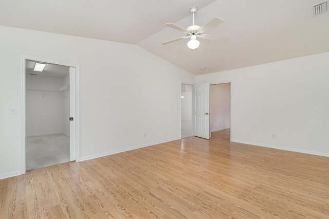 unfurnished bedroom with lofted ceiling, light hardwood / wood-style flooring, a walk in closet, ceiling fan, and a closet