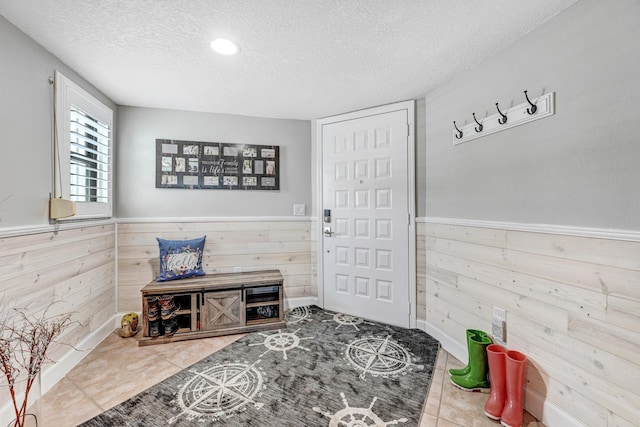 foyer with tile patterned floors, wooden walls, and a textured ceiling