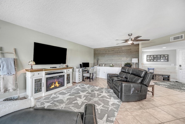 living room with light tile patterned floors, ceiling fan, a textured ceiling, and wood walls