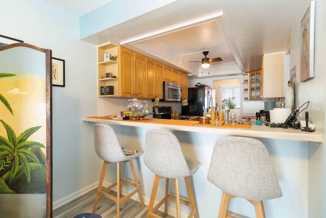 kitchen featuring a kitchen bar, ceiling fan, kitchen peninsula, stainless steel appliances, and light hardwood / wood-style flooring
