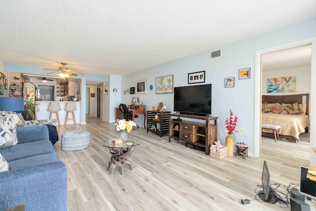 living room with ceiling fan, light hardwood / wood-style flooring, and a textured ceiling