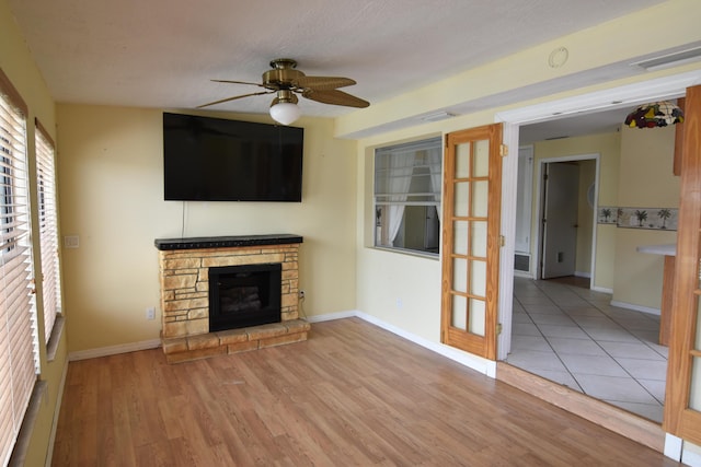 unfurnished living room featuring a textured ceiling, ceiling fan, light hardwood / wood-style floors, and a fireplace