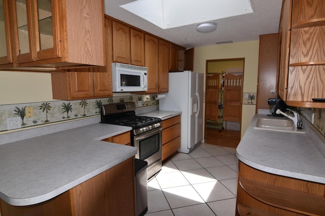 kitchen featuring a skylight, sink, kitchen peninsula, white appliances, and light tile patterned floors