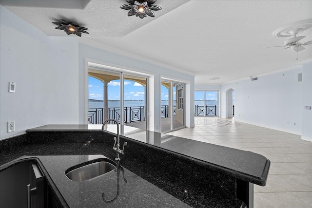 kitchen with dark stone countertops, light tile patterned floors, sink, ceiling fan, and a textured ceiling