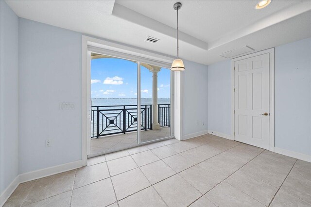 tiled spare room featuring a tray ceiling and a water view