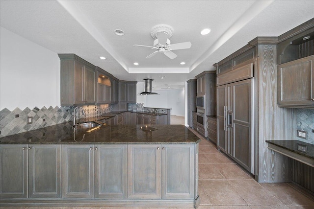 kitchen featuring sink, a raised ceiling, kitchen peninsula, dark stone counters, and ceiling fan