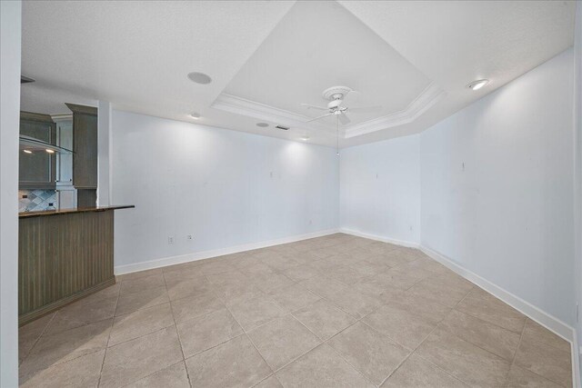 tiled spare room featuring a tray ceiling, crown molding, and ceiling fan