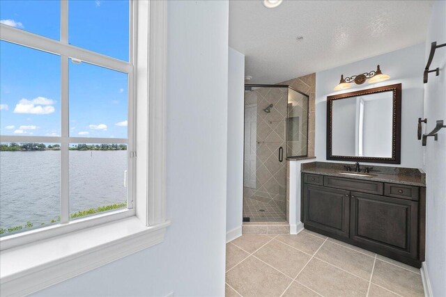 bathroom featuring a shower with shower door, vanity, tile patterned floors, and a water view