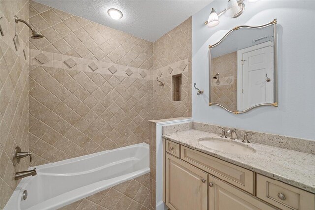 bathroom with tiled shower / bath, a textured ceiling, and vanity