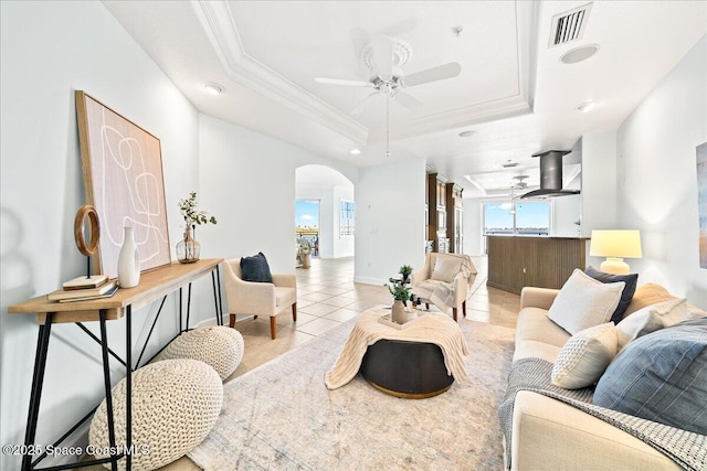 living area with light tile patterned floors, visible vents, arched walkways, a tray ceiling, and crown molding